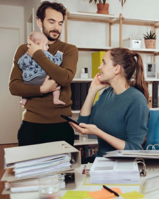 Ein junges Paar mit Kind am Reden, während die Frau im Homeoffice arbeitet.